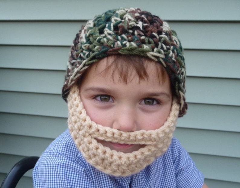 Puede incluir: Un ni&ntilde;o con un gorro de punto de camuflaje y una barba de ganchillo a juego. El gorro y la barba son de color beige y marr&oacute;n.