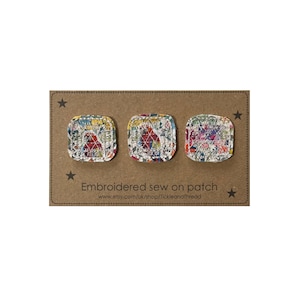 May include: Three square sew-on patches with rounded corners, featuring a multi-coloured floral and geometric pattern with white topstitching. The patches are displayed on a brown rectangular card labelled Embroidered sew on patch.