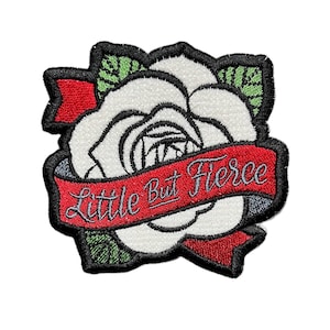 May include: Embroidered patch featuring a white rose with black outlines and green leaves. A red banner across the rose reads "Little But Fierce" in a cursive font. The patch has a black border.
