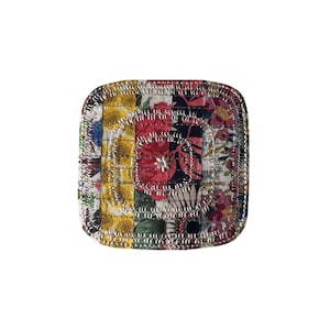 May include: Square, quilted coaster with a patchwork design. The coaster features a mix of floral and geometric patterns in red, yellow, blue, and green. The edges are finished with silver stitching, creating a decorative border.