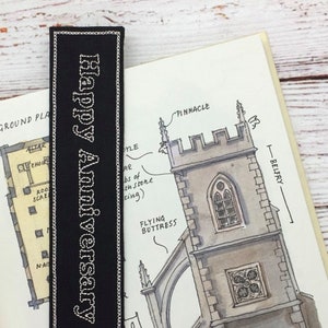 May include: Black bookmark with white stitching and the text "Happy Anniversary" embroidered in white.