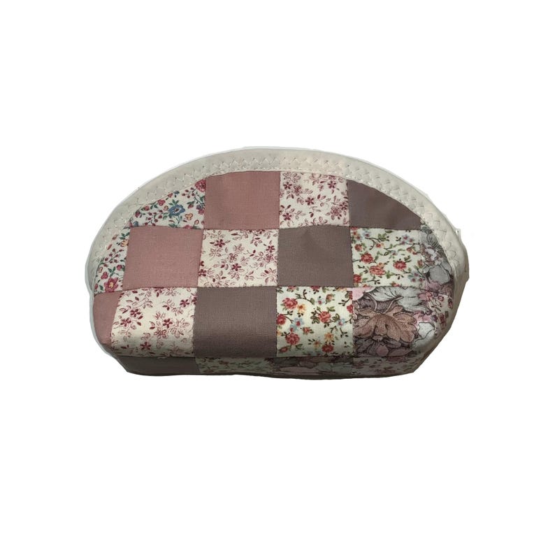 May include: An oval cosmetic bag with a patchwork design. The bag is made from squares of floral and solid fabrics in pink, brown, and cream. It has a white zip and trim, and is designed for storing makeup.