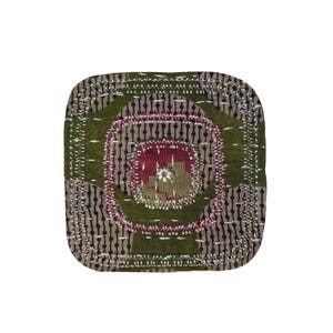 May include: Handmade square coaster with a patchwork design. The coaster has a central burgundy square, surrounded by pink and olive green circles. The edges are finished with white stitching.