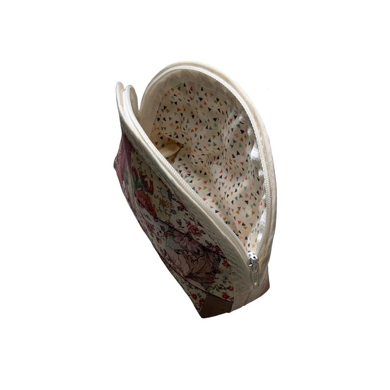 May include: A floral print cosmetic bag with a cream-coloured zip and trim. The bag's exterior features a pattern of pink and red flowers on a cream background. The interior lining has a geometric triangle pattern.