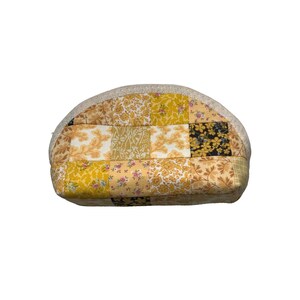 May include: A patchwork cosmetic bag with a curved top. The bag features a variety of yellow and cream-coloured floral and patterned fabrics. The top edge is trimmed with a cream-coloured fabric.