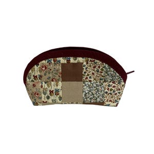 May include: A patchwork cosmetic bag with a claret-coloured zip and trim. The bag features a variety of floral and geometric patterns in beige, brown, and blue. The bag is a half-moon shape.