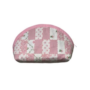May include: A pink and white quilted pouch, shaped like a half-moon. The patchwork design features alternating squares of solid pink and white floral patterns. The top edge is trimmed with solid pink fabric.