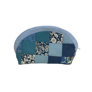 May include: A patchwork cosmetic bag in various shades of blue, with floral and solid fabric squares. The top is light blue, quilted fabric. The bag has a zip closure and is designed for storing makeup or toiletries.