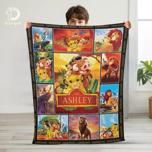 May include: A rectangular blanket featuring scenes from "The Lion King" movie. The blanket has a black border with the words "LION KING" repeated. The center features various characters and the name "ASHLEY".
