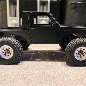 May include: Black toy truck with a white interior and black wheels. The truck has a black bed and a black cab with a single door. The truck has a "3L" logo on the side.
