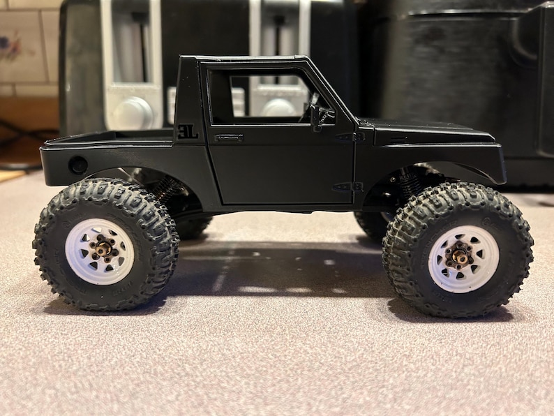May include: Black toy truck with a white interior and black wheels. The truck has a black bed and a black cab with a single door. The truck has a "3L" logo on the side.