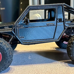 May include: A black toy truck with a roll cage and red wheels. The truck has a black body and a black interior. The truck is sitting on a gray surface.