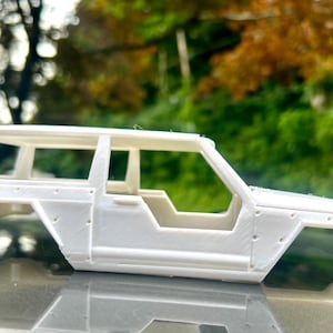 以下が含まれることがあります： 白いプラスチック製のモデルカーのシャーシ、取り外し可能な屋根が付いた4ドアSUVの、詳細な未塗装のボディシェルです。
