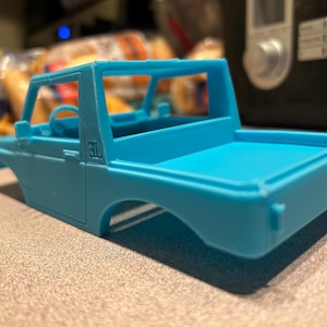 May include: A light blue plastic model car chassis with a truck bed. The model has a roll cage and a "3L" inscription on the side.