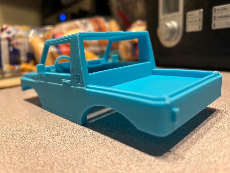 May include: A light blue plastic model car chassis with a truck bed. The model has a roll cage and a "3L" inscription on the side.