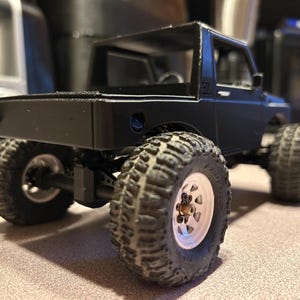 May include: Black toy truck with a white rim and black tires. The truck has a black bed and a black roll cage.