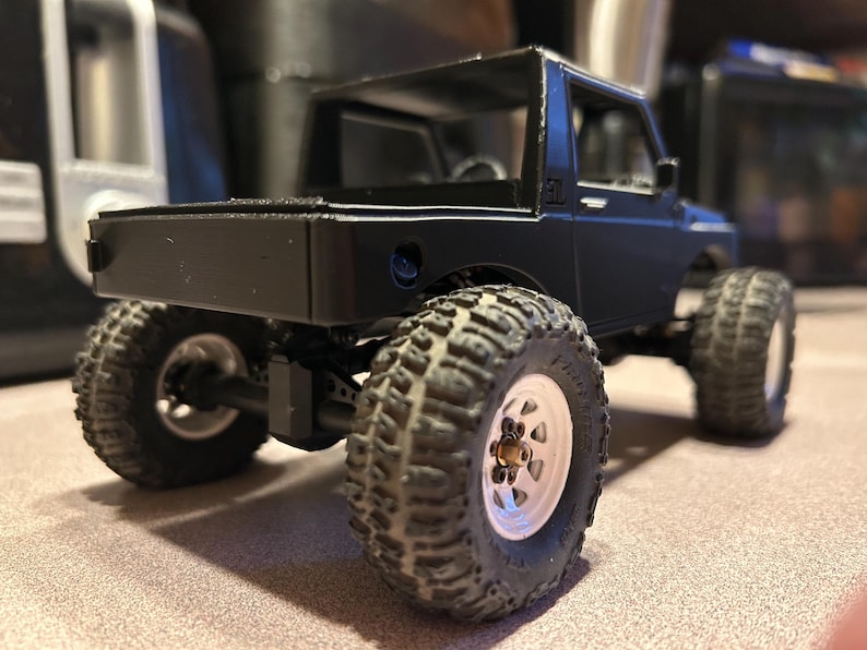 May include: Black toy truck with a white rim and black tires. The truck has a black bed and a black roll cage.