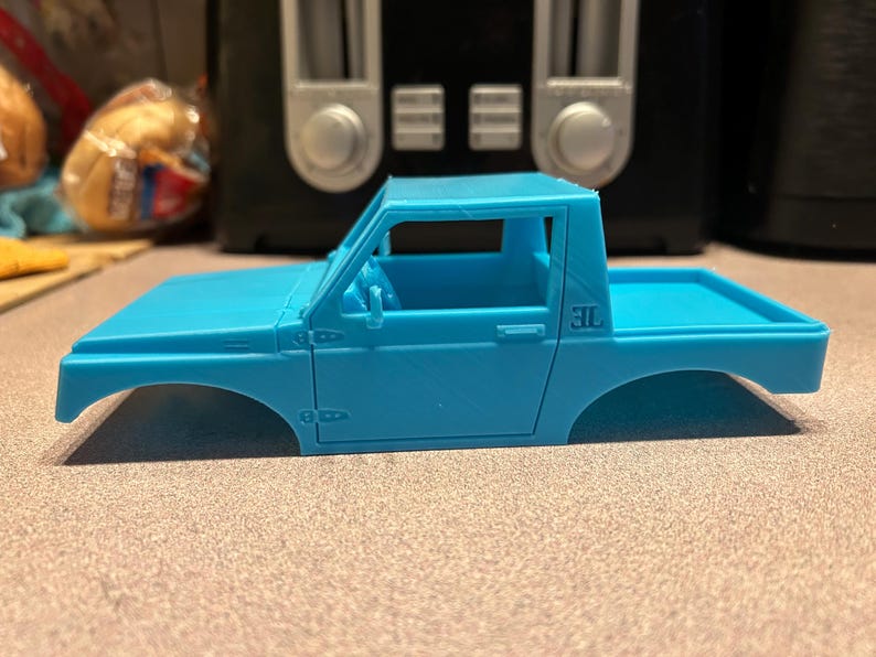 May include: A light blue plastic model car body, a pickup truck with a single cab and a flatbed. The model has a door on the driver's side and a 3L printed on the bed.