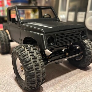 May include: Black and grey toy truck with a black grill and black wheels. The truck has a black interior and a black frame.