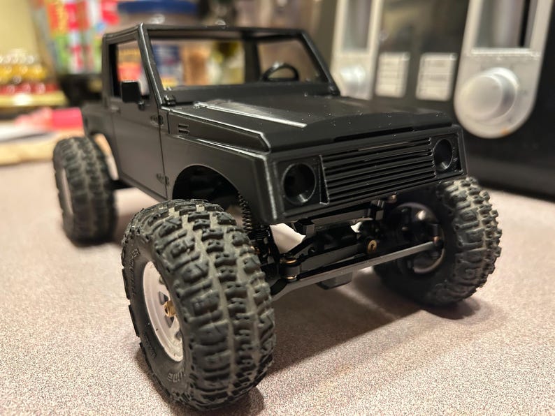 May include: Black and grey toy truck with a black grill and black wheels. The truck has a black interior and a black frame.