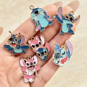 May include: A collection of colorful enamel charms featuring the character Stitch from the Disney movie Lilo & Stitch. The charms are in various poses and colors, including blue and pink, with gold-colored metal accents.