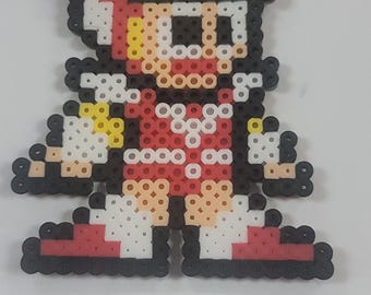 May include: Pixel art figure of a character in a red racing suit, yellow helmet, and black and white checkered flag on the head. The figure is made of small, colorful beads. The figure is standing on a white surface.