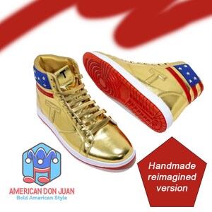 Puede incluir: Zapatillas doradas de ca&ntilde;a alta con detalles rojos y blancos y un dise&ntilde;o de bandera estadounidense azul y blanca en la parte posterior. Las zapatillas tienen una suela blanca y una franja roja alrededor de la parte superior. El texto "Handmade reimagined version" es visible en la imagen.