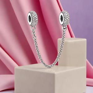 Può includere: Catena di sicurezza per charm color argento con due charm rotondi con pavé. Ogni charm è incastonato con piccoli cristalli trasparenti. Gli charm sono collegati da una delicata catena, progettata per evitare la perdita di gioielli.