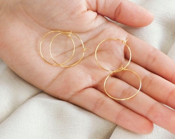 May include: Three gold hoop earrings on a hand. The earrings are simple and delicate.