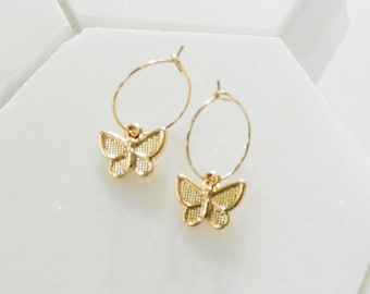 May include: A pair of gold hoop earrings with a butterfly charm hanging from each hoop.