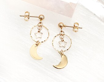 May include: Gold earrings with a crescent moon and star charm. The earrings are dangling and have a simple design.