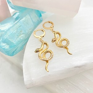 May include: A pair of gold snake earrings with clear stones. The snakes are coiled and have a small red stone for an eye.