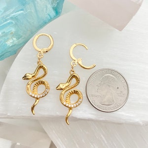 May include: Gold snake hoop earrings with clear crystal accents. The earrings are approximately the size of a US quarter.