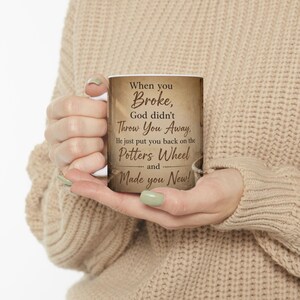 May include: A white ceramic mug featuring a vintage-style parchment background with dark brown text that reads: When you Broke, God didn't Throw You Away, He just put you back on the Potters Wheel and Made you New! The mug has a curved handle.