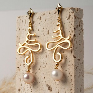 以下が含まれることがあります： ゴールドカラーのドロップイヤリングのペア。各イヤリングは、上部に小さなダイヤモンドアクセント、下部にぶら下がっているパールが付いた、様式化された渦巻きデザインが特徴です。片方のパールはソフトピンク、もう片方は白です。