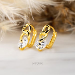 May include: Gold hoop earrings with a dangling chain design and a clear cubic zirconia stone.