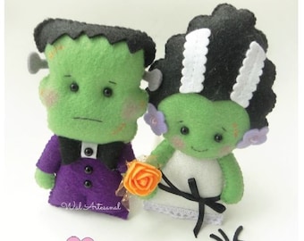 May include: A green Frankenstein couple doll set. The male doll is wearing a purple suit with a black bow tie. The female doll is wearing a white dress with a black sash and a white lace trim. The dolls are holding a single orange flower. The text "Frankenstein Couple" is on a pink sign.