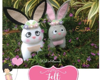 May include: Two felt bunny rabbit toys with flower crowns. The bunny on the left is white with black ears and the bunny on the right is gray with pink ears. The bunnies are sitting in a bed of pink flowers. The text "Happy Easter" is written in white on a pink background.