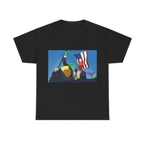 Puede incluir: Una camiseta negra con un estampado gráfico de cuatro personajes de dibujos animados sosteniendo una bandera estadounidense. Los personajes son verdes, amarillos, rojos y morados.