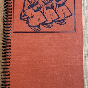 May include: A red spiral bound notebook with a blue illustration of three monks reading books on the front cover.