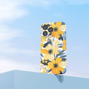 May include: A phone case with a floral design featuring large yellow flowers with black centers and gray leaves on a white background. The case has a glossy finish and is set against a blue sky.