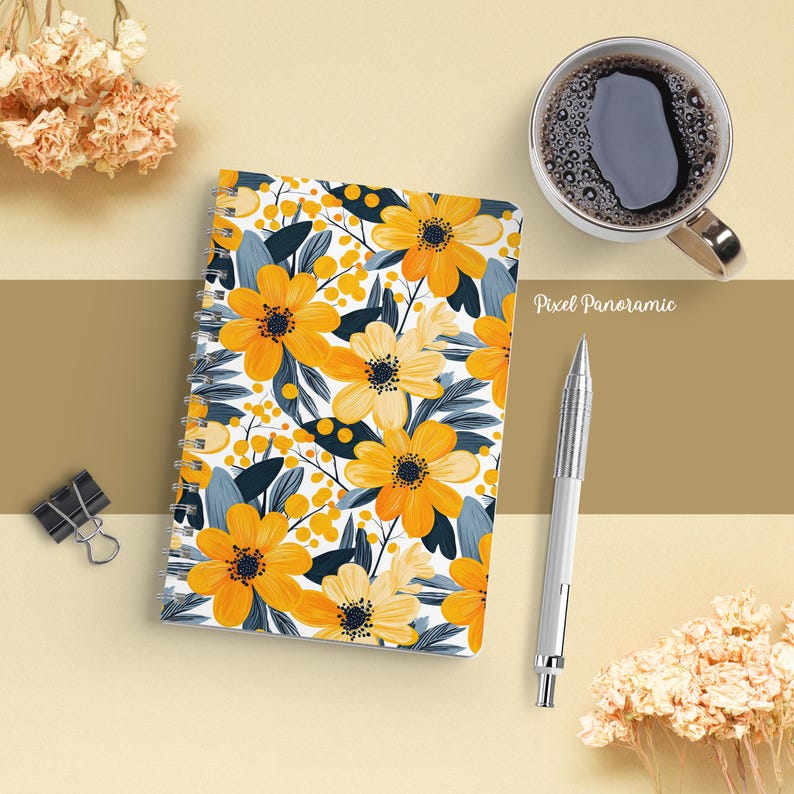 May include: A spiral-bound notebook with a floral design featuring large yellow flowers, dark blue leaves, and small yellow berries on a white background. A silver pen and a cup of coffee are next to the notebook.