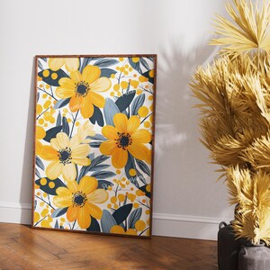 May include: A framed floral print featuring a vibrant yellow flower design with dark blue-green leaves and small yellow berries against a white background. The artwork is in a wooden frame and leans against a white wall.