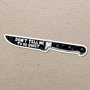 Puede incluir: Una pegatina en blanco y negro con forma de cuchillo. La pegatina tiene el texto "DON'T TELL ME TO BE QUIET" en letras blancas en negrita. El cuchillo tiene un mango y una hoja negros.