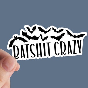 Puede incluir: Una pegatina blanca con una silueta negra de murciélagos y el texto "BATSHIT CRAZY" en negro.