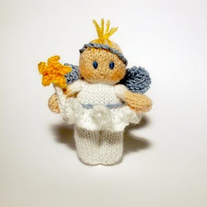 May include: A white knitted angel doll with a yellow star, blue wings, and a yellow crown. The doll has a sweet, innocent expression.