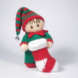 Op de afbeelding: Een gebreide elfenpop met een groen-rode gestreepte muts, een groen-rode outfit en een rood-witte sok.