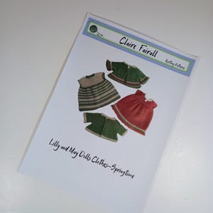 May include: A printed knitting pattern document titled Claire Fairall Knitting Patterns, featuring illustrations of four knitted doll garments: a striped dress, a red dress, and two green cardigans. The text reads Lilly and May Dolls Clothes-Springtime.