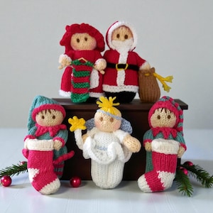 May include: A collection of five hand-knitted dolls featuring Santa Claus, Mrs. Claus, an angel with a yellow star, and two elves. The figures are crafted with yarn in red, white, green, and blue, with detailed facial features and holiday accessories.
