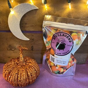 Puede incluir: Una bolsa de plástico transparente llena de maíz dulce de colores y otros dulces con temática de Halloween. La bolsa tiene una etiqueta morada que dice "Spellbound Sweets and Treats Est. 2024" y "Spooky Peep Autumn Mix".